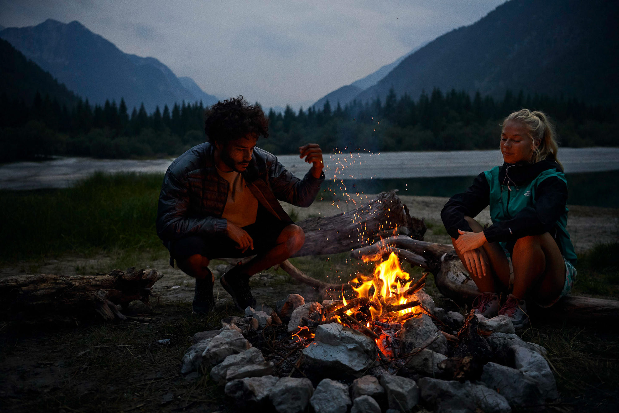Hikers sitting around a campfire by a mountain lake in Slovenia
