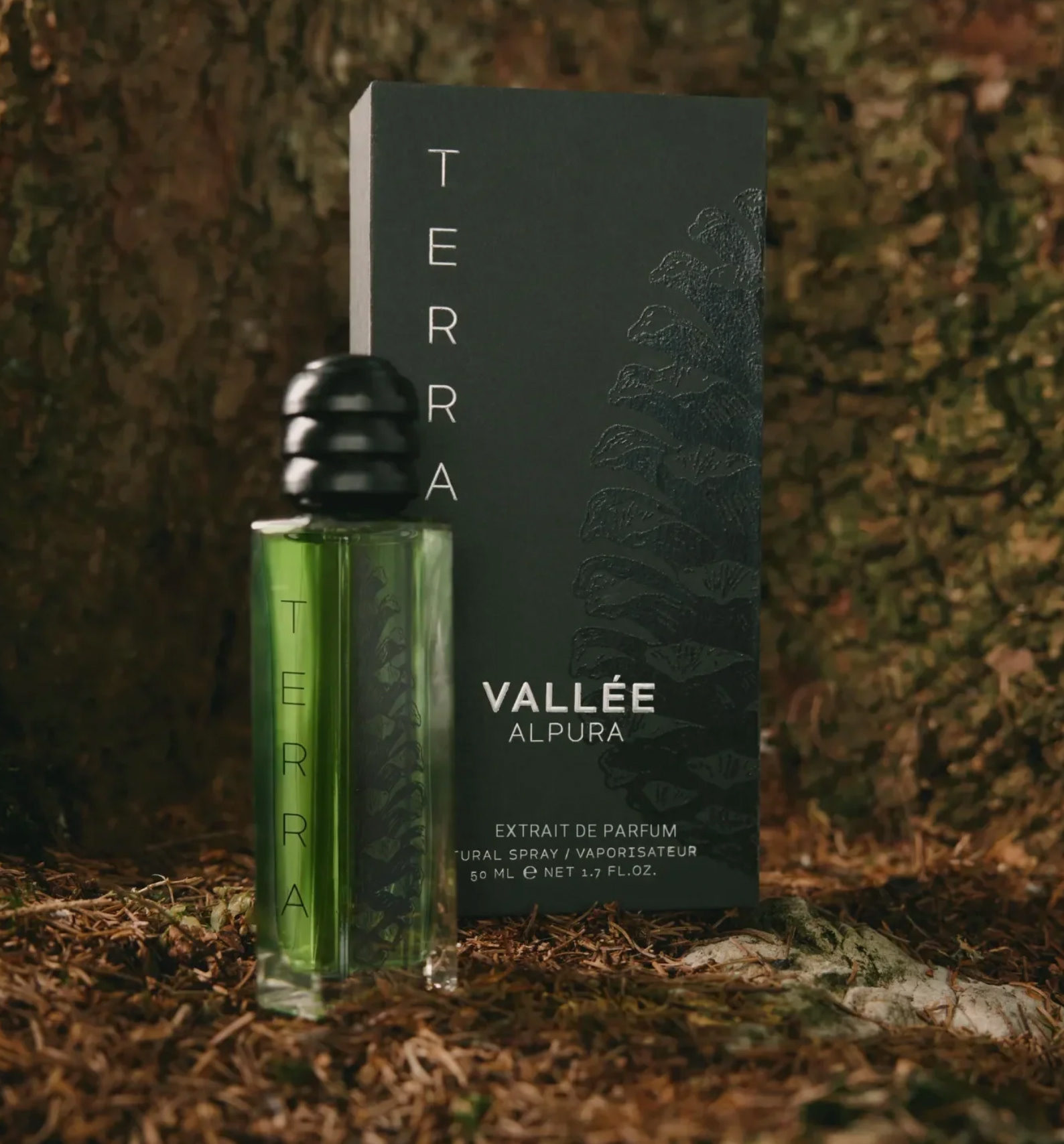 Green Valée Alpura fragrance bottle photographed outdoors in an Alpine forest setting; product shot