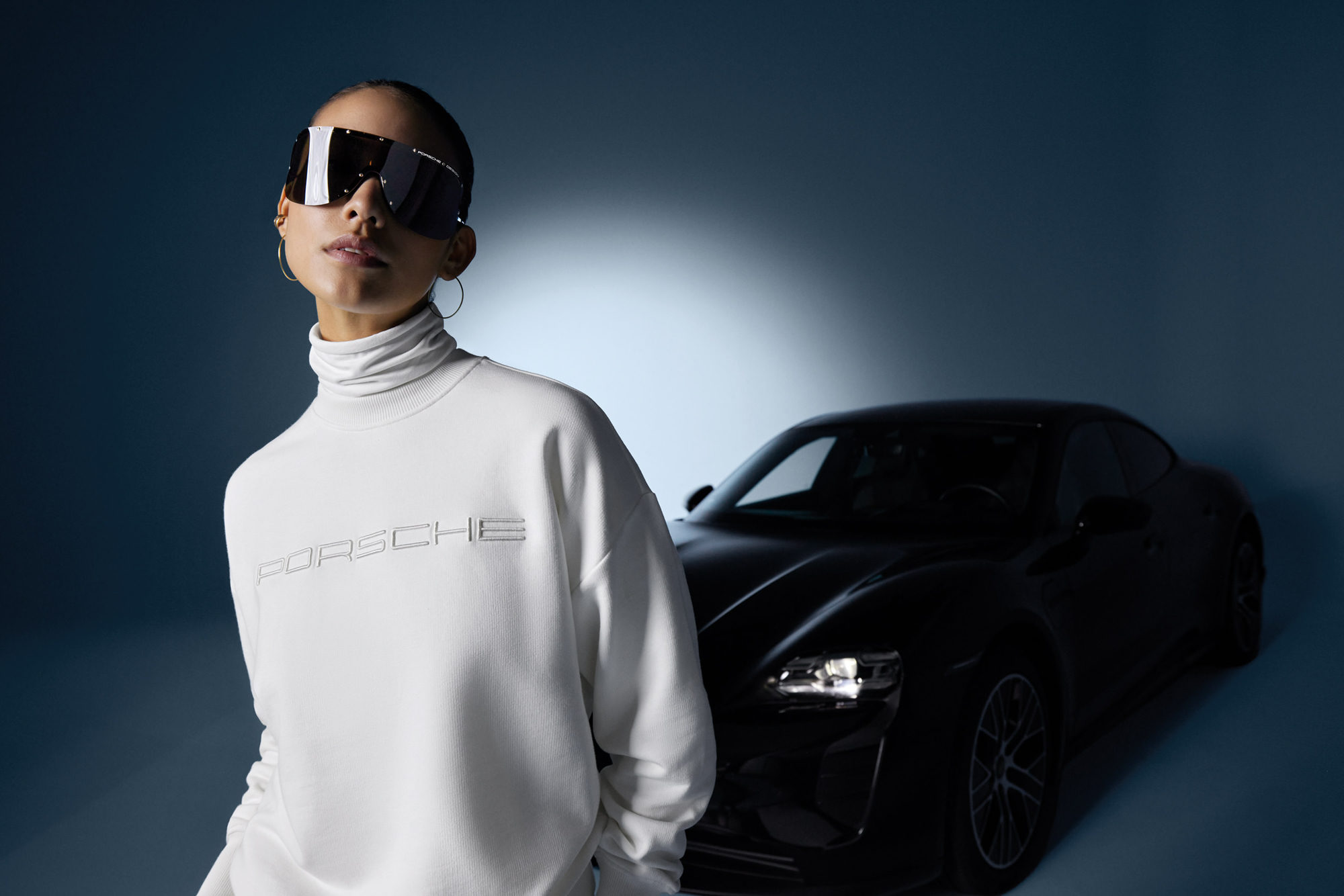 female model in white Porsche Design sportswear standing in front of a black sports car