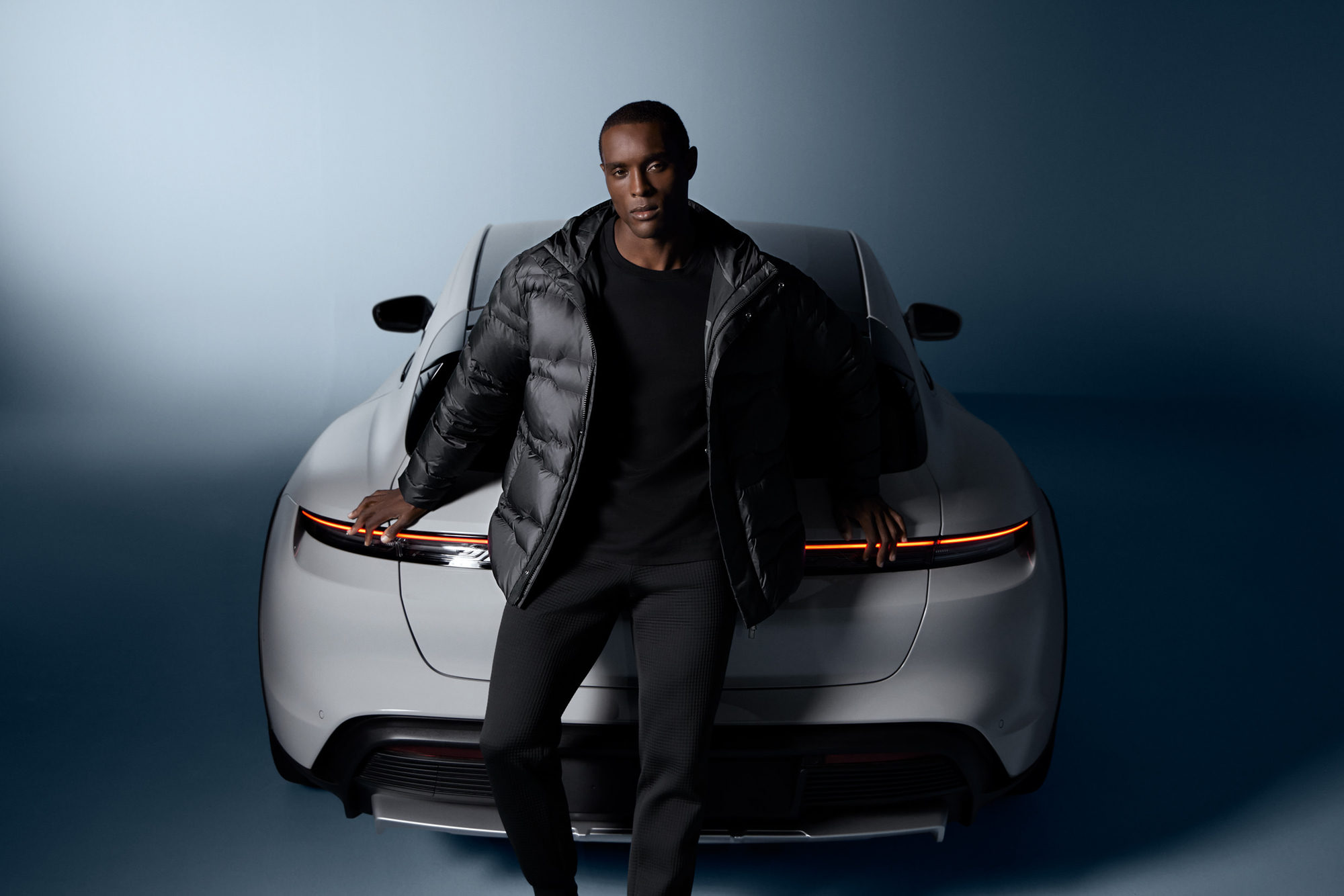 male coloured model in black Porsche Design sportswear posing in front of a white porsche sports car