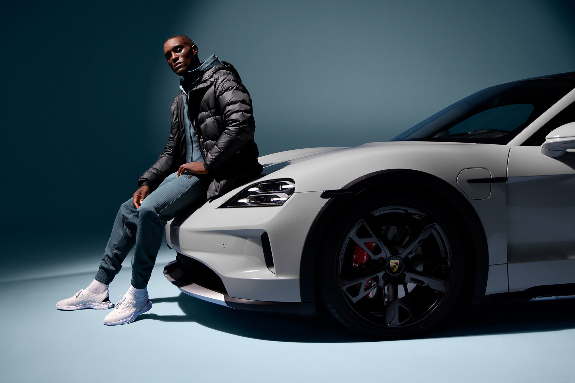 coloured model in Porsche Design wear in front of a white porsche sports car in a studio