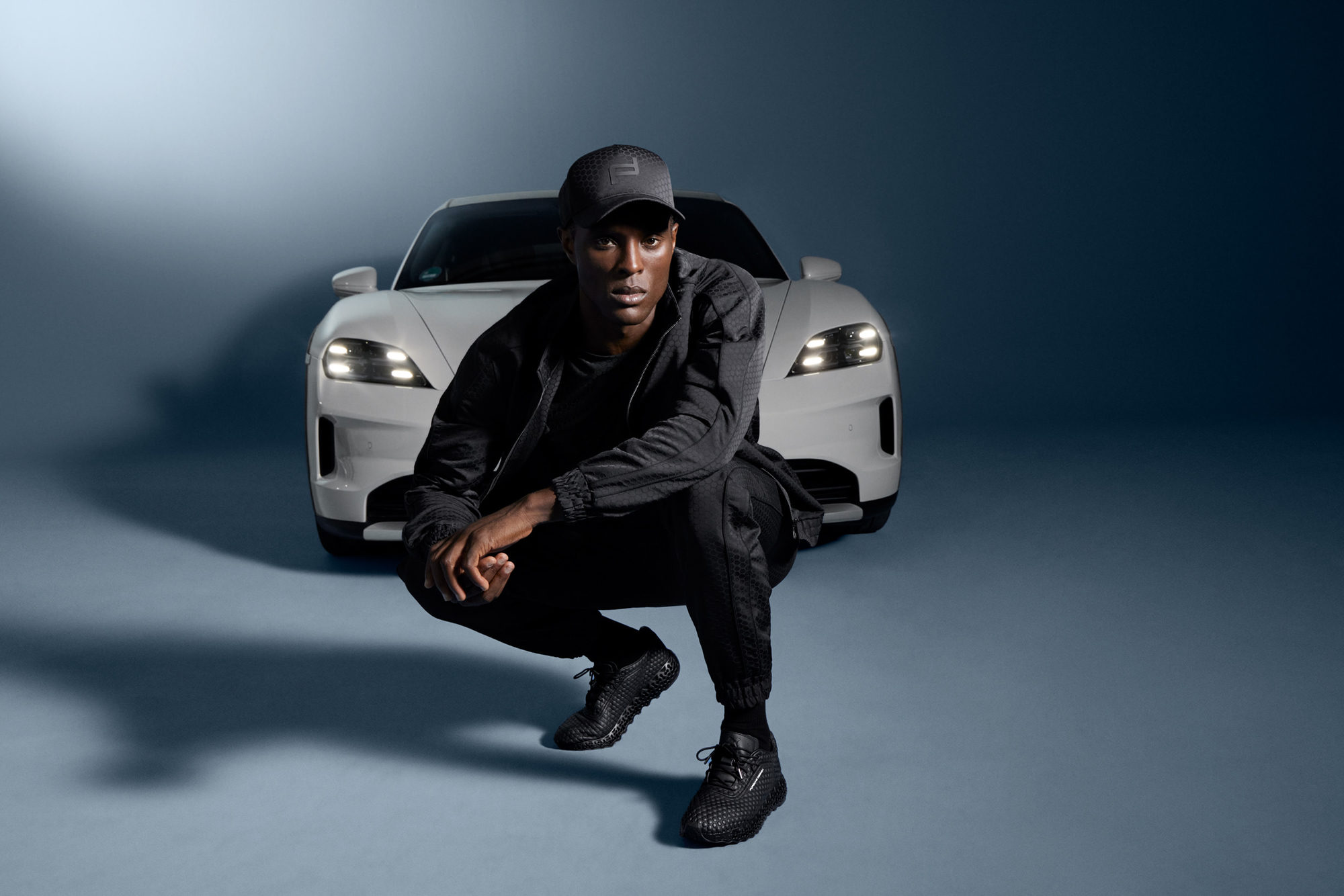 coloured model in sportswear in front of a white porsche sports car in a studio