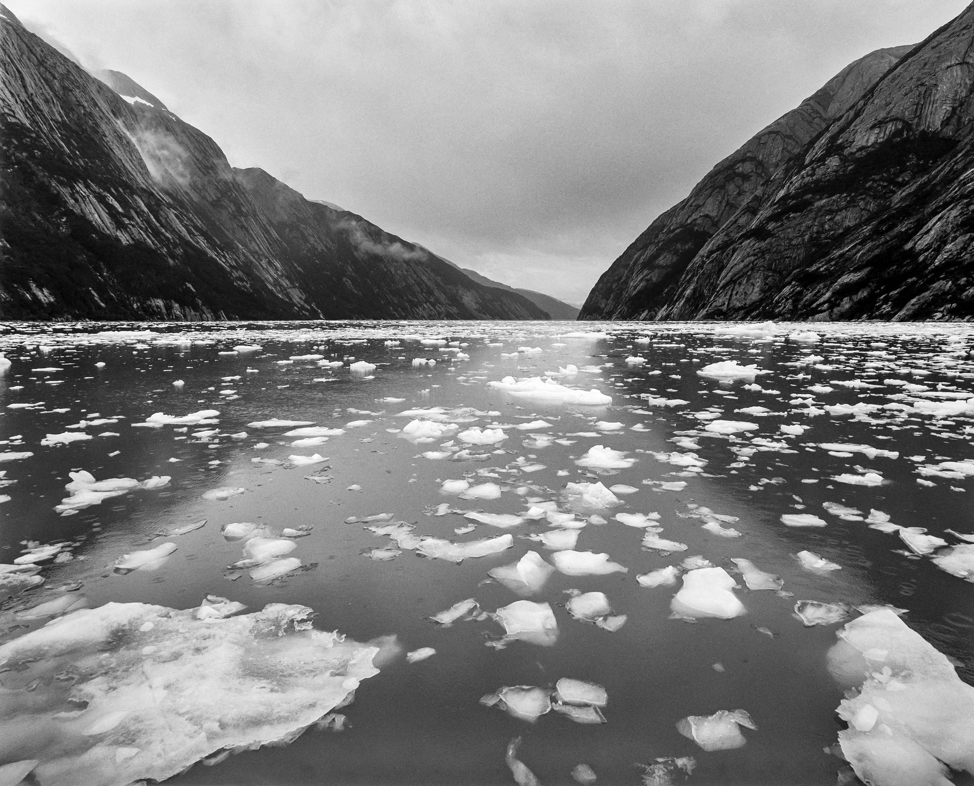 Black-and-white photograph of ice floes drifting between steep mountains in the Beagle Channel, Tierra del Fuego.