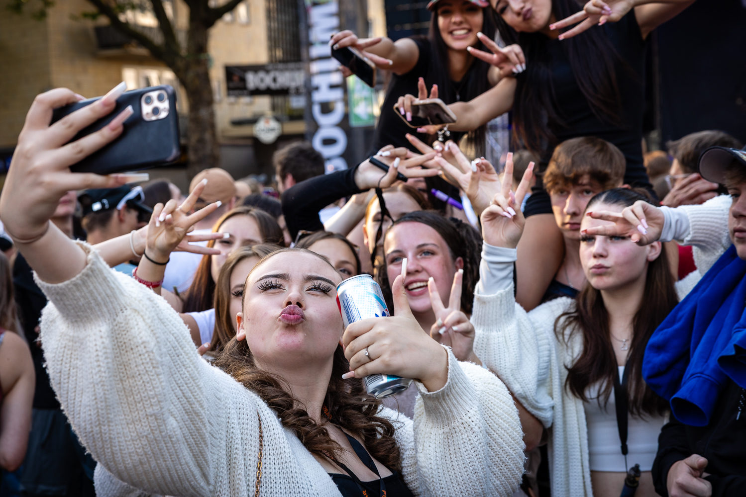 Young people taking selfies with smartphones in a crowded public space.