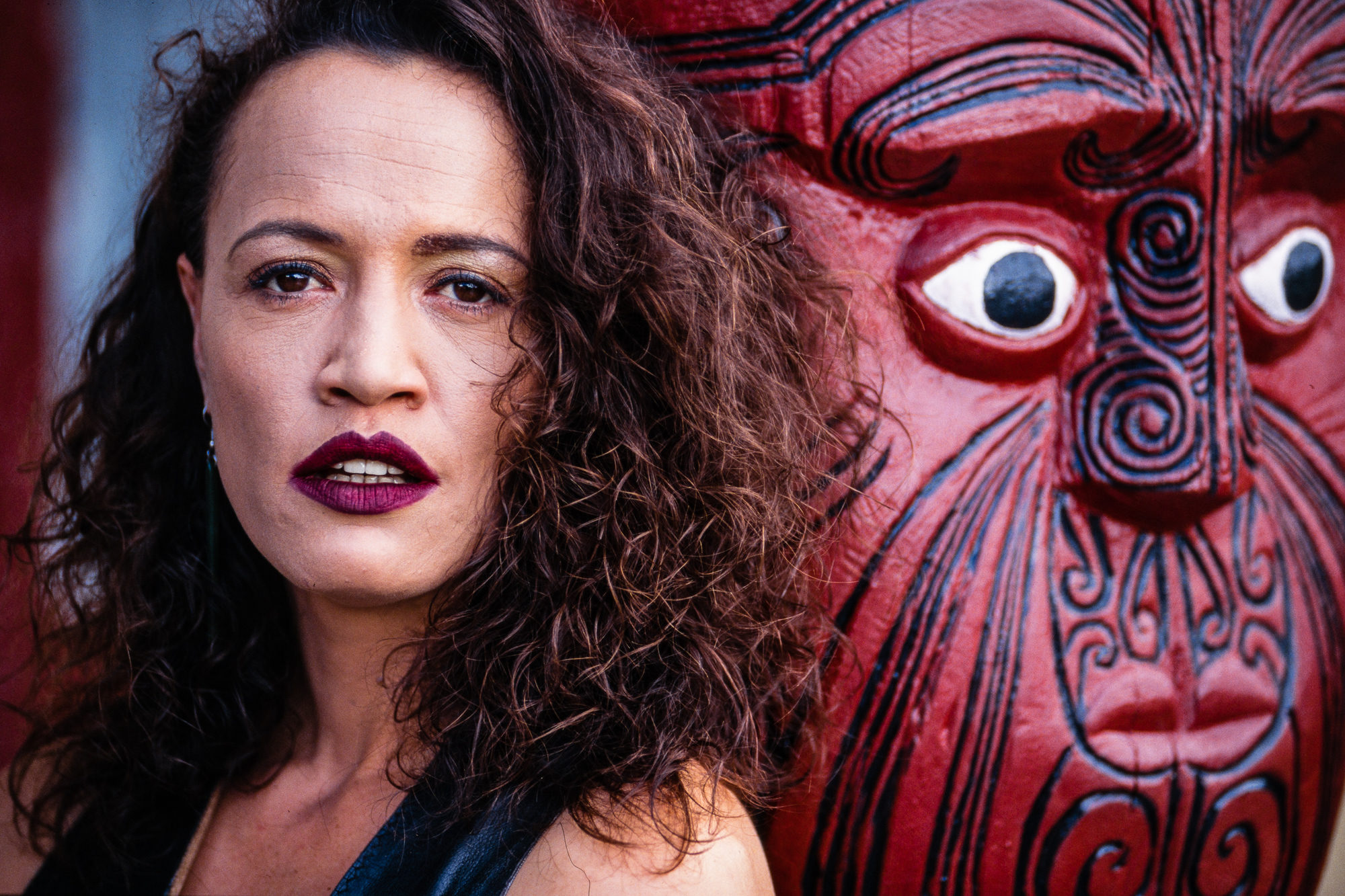 Rena Owen — Portrait of Rena Owen standing outdoors beside a large red Māori figure in Paihia, New Zealand.
